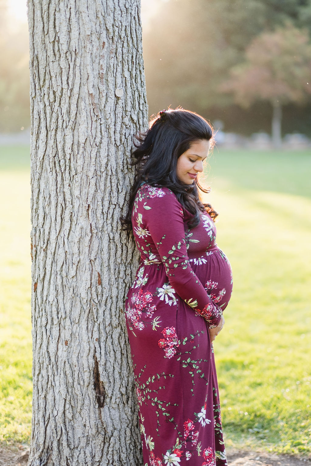 pregnant woman leaning against tree looking at her stomach