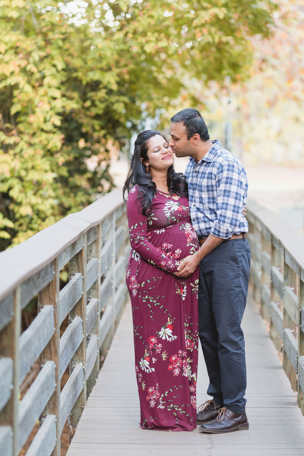 husband kissing his pregnant wife on a rustic bridge